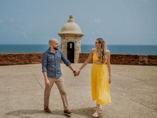 A smiling couple holds hands on top of a castle with a view of the ocean 