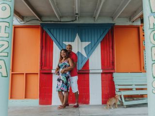 A couple embraces in front of a painted wall with the flag of Puerto Rico on it 