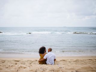 A couple sits together on a beach looking at the ocean 