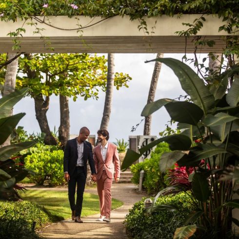 Smiling couple in suits walk hand-in-hand through tropical garden